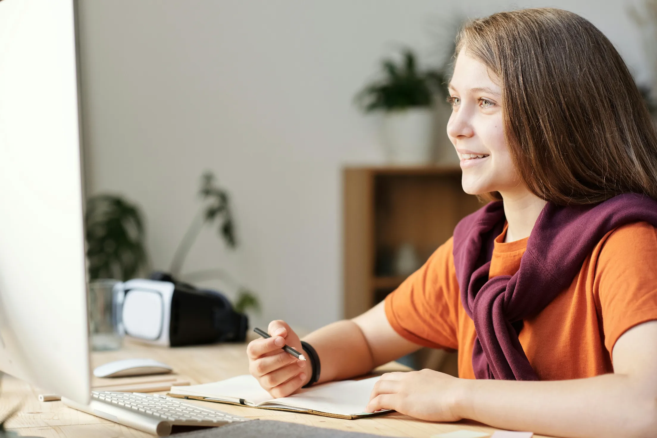 A smiling student writing notes by hand in a notebook at her desk